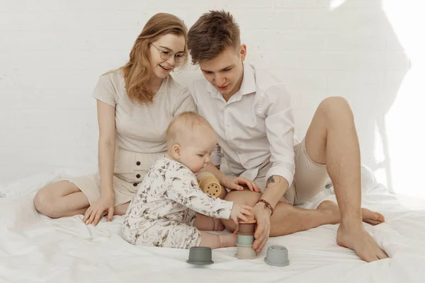 Jovem família bonita sorridente com bebê bebê querúbico brincando com modernas tigelas de silicone pastel de tamanho diferente. — Fotografia de Stock