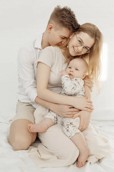 Beyaz elbiseli gülümseyen genç bir ailenin portresi. Küçük, tombul, mavi gözlü bebek bebek oturuyor.. — Stok fotoğraf