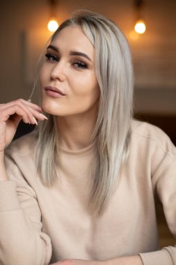 Dikey, güzel, çekici, sarışın, makyajlı, bej kazaklı, kameralı, civcivini tutan bir kadın.