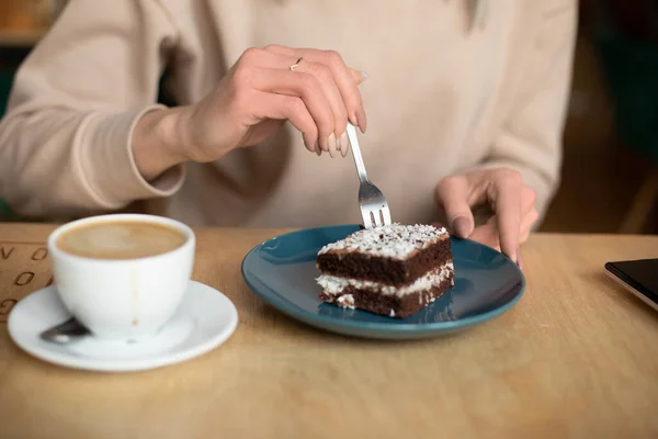 Foto tangan wanita yang dipotong di kafe warung kopi, makan brownies lezat bubuk gula. Secangkir kopi di atas meja kayu. — Stok Foto