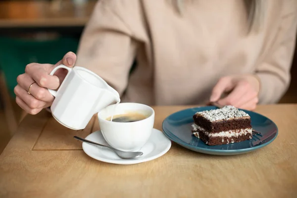 Foto yang dipotong dari wanita kabur menuangkan susu krim di kopi, makan kue brownies. Cafe liburan kesenangan, menutup — Stok Foto