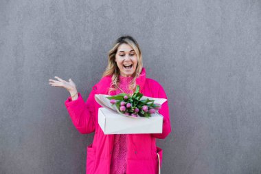 Gülen mutlu sarışın kadının portresi pembe bir buket lale çiçeği ve hediye kutusu alıyor. Gri görünüm