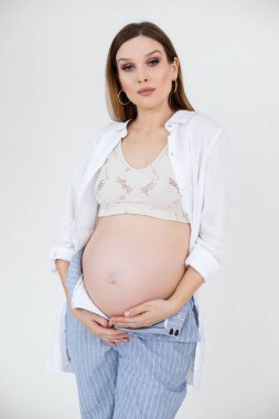 Çekici, kendine güvenen, makyajlı hamile bir kadının dikey fotoğrafı. Karnını, karnını tutuyor. Anne sağlık hizmetleri,