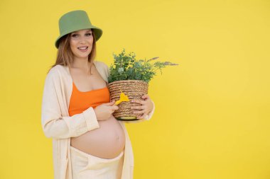 Yeşil şapkalı, turuncu bluzlu ve saksısı olan hamile bir kadının portresi. Tarım ve bakım yeşili