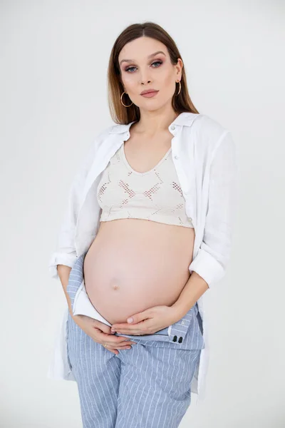 Verticale foto van aantrekkelijke, zelfverzekerde zwangere vrouw in top, met make-up. Buik, buik vasthouden. Gezondheidszorg voor moeders, — Stockfoto