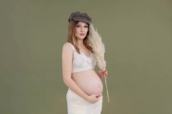 Modieuze zwangere vrouw vlas pet, kant outfit. Ontroerende buik. Het voorbereiden van zwangerschap ouderschap, met decoreren borstel — Stockfoto