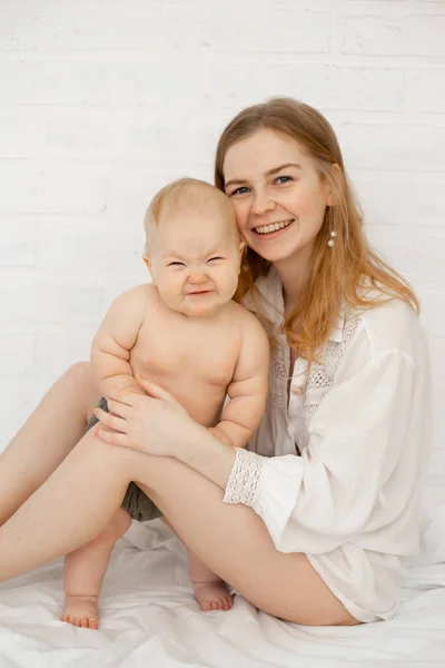 Beyaz yatak odasında çıplak ayaklı sarışın bir kadının çıplak bebekle dikey hali. Temizlik prosedürlerinden sonra. Anne ilgileniyor. — Stok fotoğraf