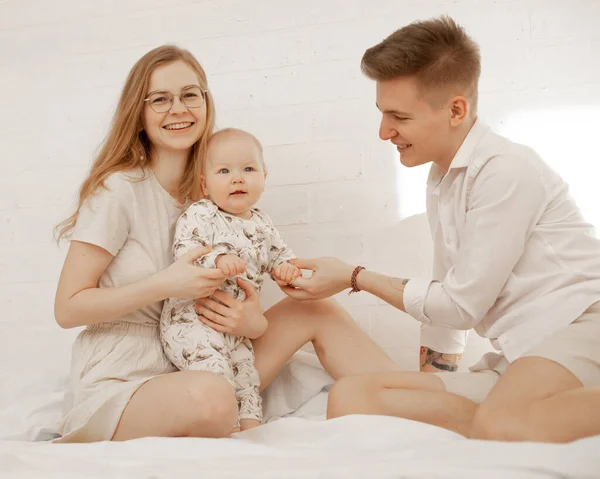白いベッドスプレッドに横たわっている女性、男性と乳児の赤ちゃんの幸せな家族。健康的な生活様式。手のマッサージ — ストック写真