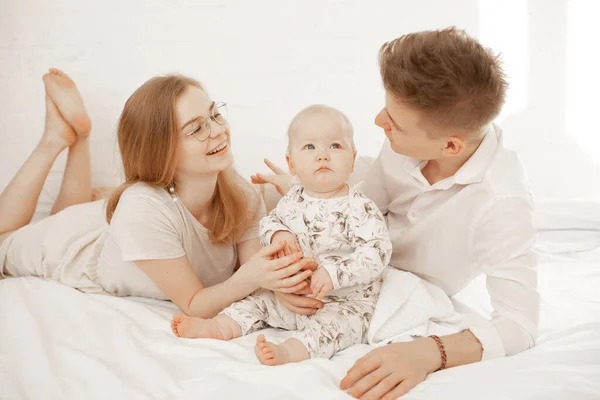 Щаслива радісна задоволена сім'я жінки, чоловіка і немовляти, що лежить на білому ліжку. Сімейний день разом, ігри з дитиною — стокове фото