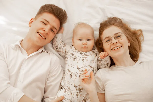 Retrato de feliz alegre casal alegre, criança recém-nascida, deitado na cama branca em cobertor. Mãe, pai. Objetivos familiares vinculados — Fotografia de Stock