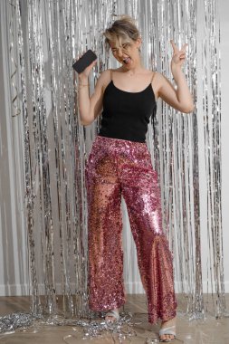 Dikey mutlu sarışın kadın, bağırıyor, zaferini gösteriyor. Doğum gününü kutlamak, yeni modern akıllı telefon hediyesi. Lametta