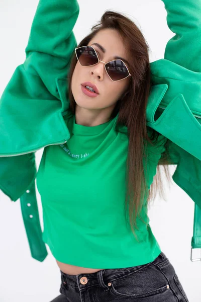 Portrait of young lady in black jeans, green jacket and t-shirt with sunglasses. Attractive woman with trendy accessory and stylish wear closeup. Fashion photo, posing on white background in studio — Stock Photo, Image