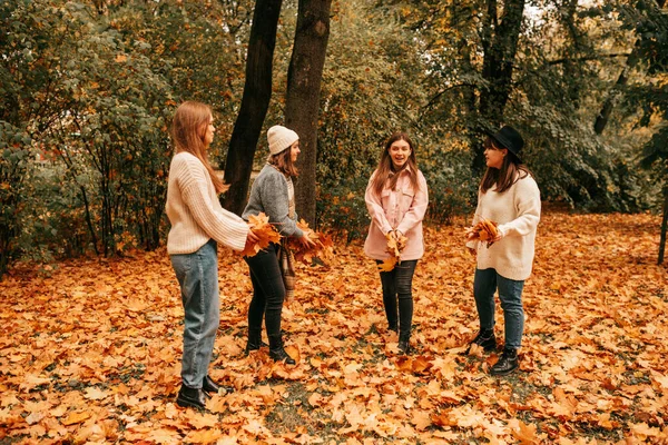四个年轻女子留下来准备向空中扔枫叶。玩的开心，在橙色的秋天公园里散步 — 图库照片