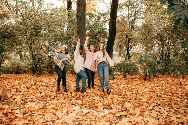 Four close female friends company hang out, spending time together in maple park. Throwing maple leaves in the air