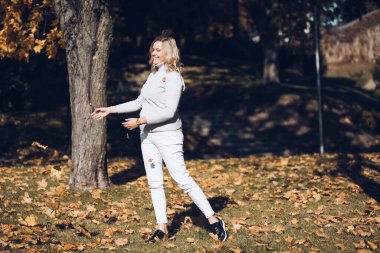 Sarışın, gülen bir kadın, açık havada eğlenen, spor aktiviteleri yapan sarı yapraklı akçaağaçlar. Ağaç kabuğu