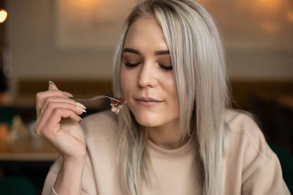 Potret wanita muda yang menarik hati dengan rambut abu-abu panjang memegang garpu dengan sepotong kue dengan mata tertutup di kafe. — Stok Foto