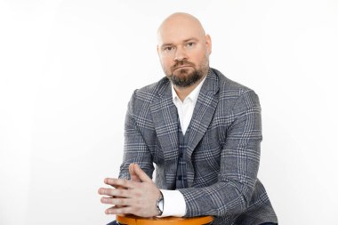 Gri kareli ceketli, beyaz gömlekli, taburede oturmuş poz veren orta yaşlı yakışıklı iş adamının portresi..