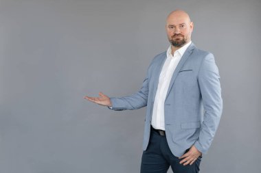 Mavi ceket, pantolon, beyaz gömlek giyen, ayakta duran, düz avuç içiyle elini kaldıran orta yaşlı bir adamın portresi..