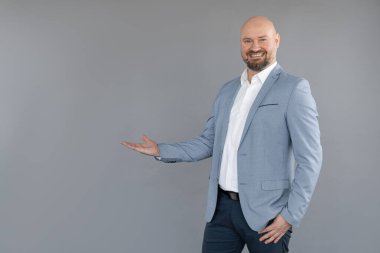 Mavi ceket, pantolon, beyaz gömlek giyen, ayakta duran, düz avuç içiyle elini kaldıran orta yaşlı bir adamın portresi..