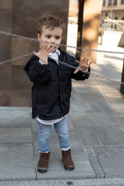 Foto verticale di bambino carino in giacca nera in piedi sulla strada, tenendo le catene. Anomalie dello sviluppo — Foto Stock