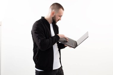 Siyah ceketli, kot pantolonlu, beyaz tişörtlü, dizüstü bilgisayar kullanan kısa saçlı, meşgul bir genç..