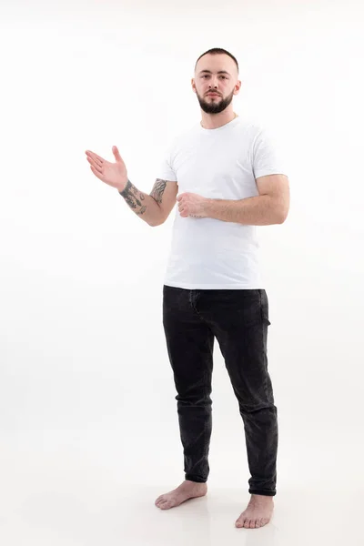 Ritratto di giovane uomo barbuto con capelli corti e scuri in T-shirt bianca, jeans neri, alzata della mano con palmo aperto. — Foto Stock