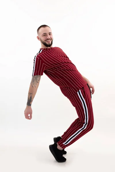 Joven hombre barbudo sonriente feliz con pelo corto oscuro en ropa deportiva de rayas rojas, zapatillas negras, posando de pie en los dedos de los pies. — Foto de Stock