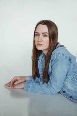 Kahverengi saçlı, doğal makyajlı ve sezonluk mavi kot ceket giyen güzel bir kadın. Genç bayanlar için günlük kıyafet kataloğu.