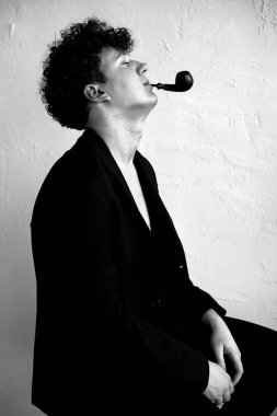 Siyah takım elbiseli, kıvırcık saçlı, pipo görünümlü, siyah beyaz fotoğraflı şık vahşi bir adam. Nikotin ve tütün bağımlısı birinin estetik portresi. Kötü alışkanlık, sağlıksız yaşam tarzı