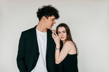 Güzel bir çift poz veriyor ve zarif siyah kıyafetler giyiyorlar. Erkekler ve kadınlar için aksesuarlar, beyaz arka plan. İş adamları için moda tarzı kıyafet kataloğu, resmi giyim eğilimleri