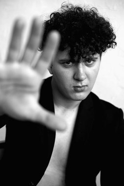 Siyah takım elbiseli, kıvırcık saçlı, eli kapalı, siyah beyaz stüdyo fotoğraflı şık, vahşi bir adam. Alışılmadık görünümlü yakışıklı birinin estetik portresi