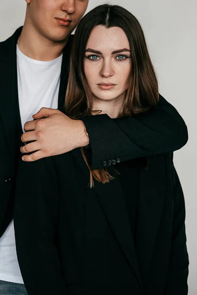 Retrato de jovem casal vestindo roupas pretas, posando. Jovem homem sério em pé atrás da mulher, abraçando com a mão. — Fotografia de Stock