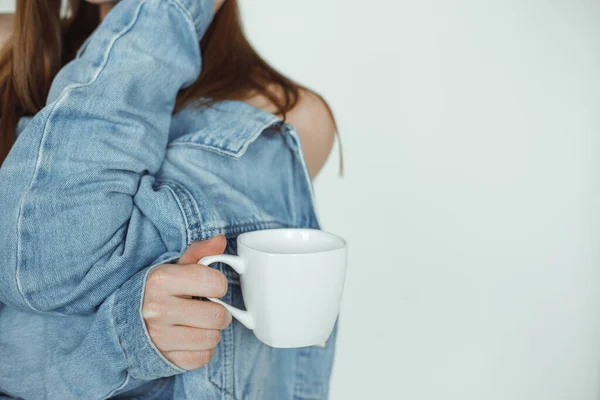 Cropped photo of woman with long dark hair wearing blue denim jacket backwards, holding white cup of coffee, posing. — Stock Fotó