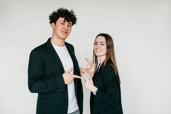 Portrait of young couple wearing black clothes. Young happy man standing near smiling woman, pointing at each other. — Stock Photo, Image