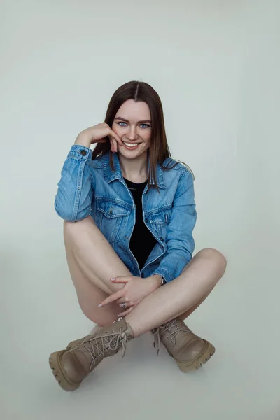 若い笑顔の肖像画良い長い暗い髪を持つ青い目の女性は、メイク、青いジャケット、ブーツを着て、座っている. — ストック写真