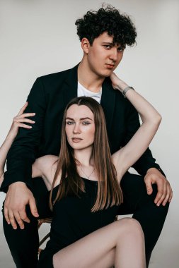 Siyah elbiseli genç bir çiftin portresi. Genç kıvırcık adam sandalyede oturuyor, ayakları üzerinde muhteşem bir kadın, sarılıyor.