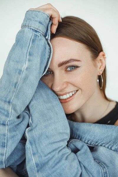 Porträtt av ung glad vacker blåögd kvinna med långt mörkt hår, smink bär blå denim jacka bakåt. — Stockfoto
