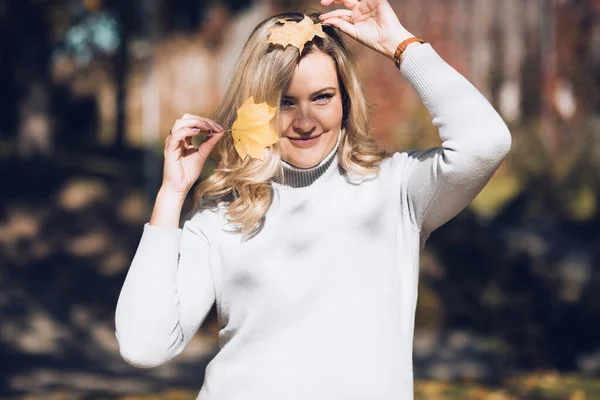 Portrait of happy woman playing with fallen foliage in autumn city park on sunny day closeup. Adult lady hold yellow leaves in hands and smile, nature background. Cozy golden autumn and weather — Stok fotoğraf