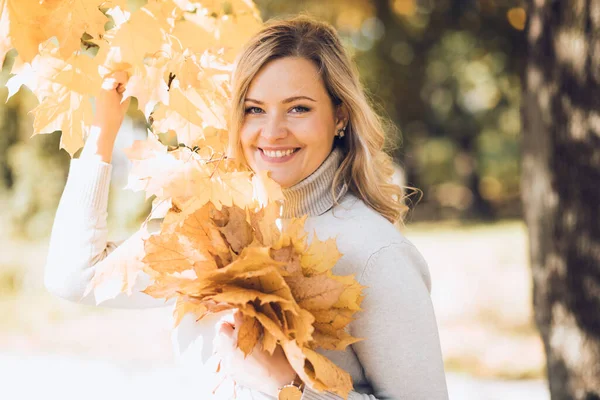 Portrait of happy woman playing with fallen leaves in autumn city park on sunny day closeup. Adult lady hold yellow foliage in hands and smile, nature background. Cozy golden autumn and weather — Stok fotoğraf