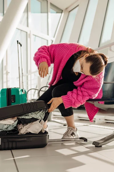 Vertical woman in pink jacket wearing face mask packing baggage sitting in waiting room at the airport. Late for flight — Stock Photo, Image