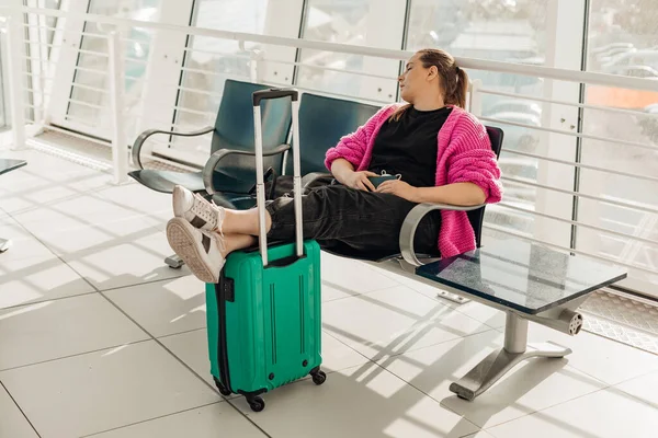 Businesswoman with luggage, keep legs on suitcase, wear pink jacket, sleep after flight in vip waiting room at airport — Stock Photo, Image