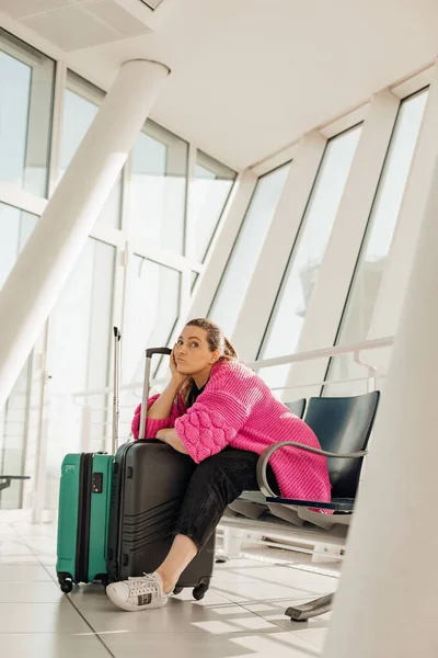 Vertical bored businesswoman leaning elbow on luggage, sitting in waiting room at airport. Flight cancellation work trip — Stock Photo, Image