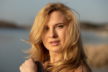 Portrait closeup of beautiful blonde woman next to river bank on cool sunny day relaxing, reflecting and enjoying peace and freedom. Outdoors weekend activity, blurred nature background