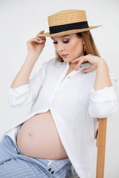 Mulher com barriga nua no final da gravidez sentar na cadeira com chapéu na cabeça, fundo branco. Retrato de jovem grávida esperando bebê closeup. Feliz gravidez e maternidade conceito — Fotografia de Stock