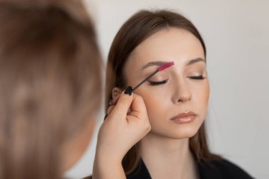 Spa salonundaki kadın yüzü, kaşlarını fırçalayıp, tarıyor, jöleli kaş çizgisi çiziyor. Parlak cilt yüzü