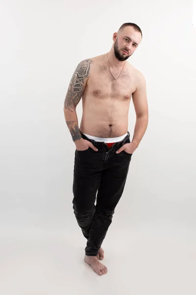 Confident handsome brutal man with beard and tattoo, shirtless and topless, on white isolated background. Look at camera — ストック写真