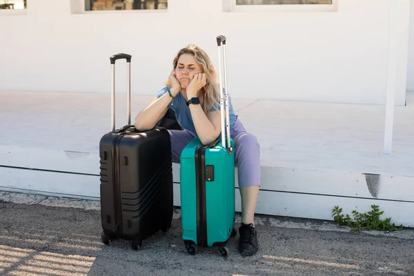 Tired, upset blond woman with luggage, lean on bags, sitting outdoors near bus station on platform, struggling of heat — Stock Photo, Image
