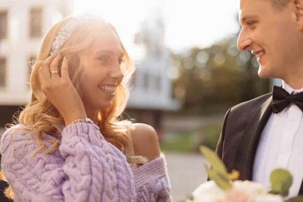 Hermosa joven pareja de boda bajo el sol en trajes elegantes caminar por la ciudad, sonreír y divertirse en el fondo de la calle. Retrato de primer plano de la novia y el novio felices en el amor. Día de la boda, vacaciones en familia — Foto de Stock