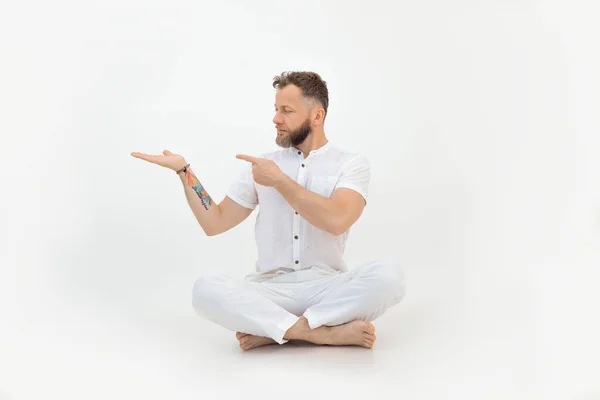 有纹身的英俊而严肃的男人坐在地板上，白色孤立的背景。手拿着空位.广告产品 — 图库照片