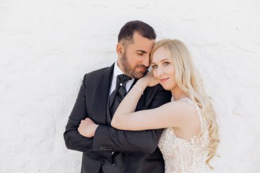 Beyaz elbiseli genç sarışın gelin portresi ve takım elbiseli esmer damat İtalya 'da caddeyi sarıp yürüyorlar. Yakın plan, beyaz duvar arka plan. Güzel ve romantik bir düğün, mutlu bir çift.